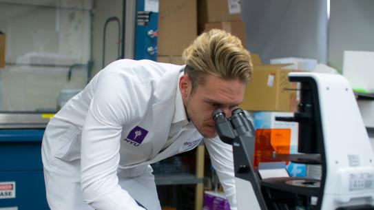 professor in lab coat looking into microscope
