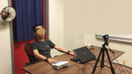 research subject wearing a headset with testing equipment and video camera on desk