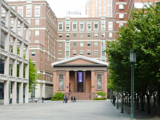 small brick building with columns surrounded by modern buildings