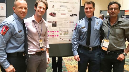 4 men (2 in uniform) standing in front of research poster