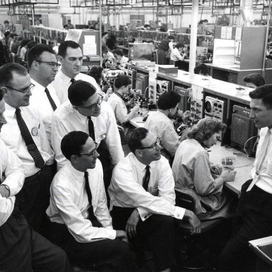 group of men in white shirts and ties sitting by woman at computer terminal