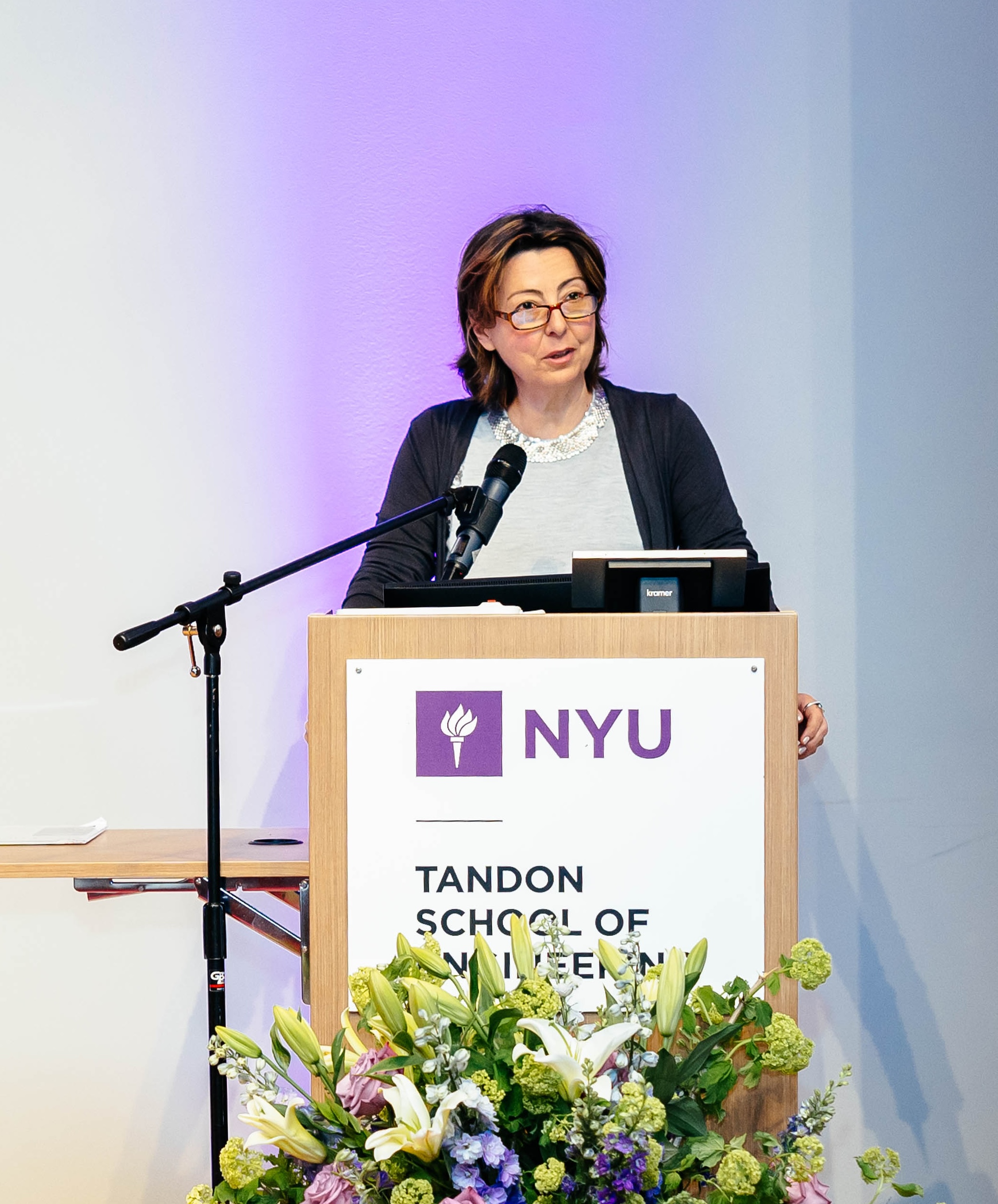 the dean speaking at a podium with floral arrangement in front